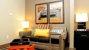 Ein Hotelzimmer mit einer Couch, einem Streifenmuster-Teppich, einer Lampe, einer Uhr und zwei gerahmten Bildern an der Wand.