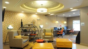 A modern hotel lobby with a seating area, a desk with computers, and a 'Business Center' sign.