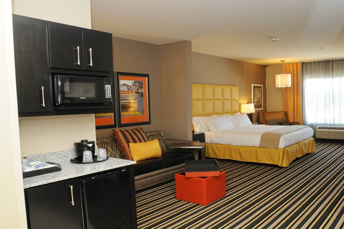 A hotel room with a bed, a desk, a microwave, a coffee maker, and a large window with curtains.
