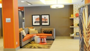 A modern hotel lobby with a sectional sofa, framed pictures on the wall, and a patterned rug. - Holiday Inn Express Covington-Madisonville by IHG (Covington)