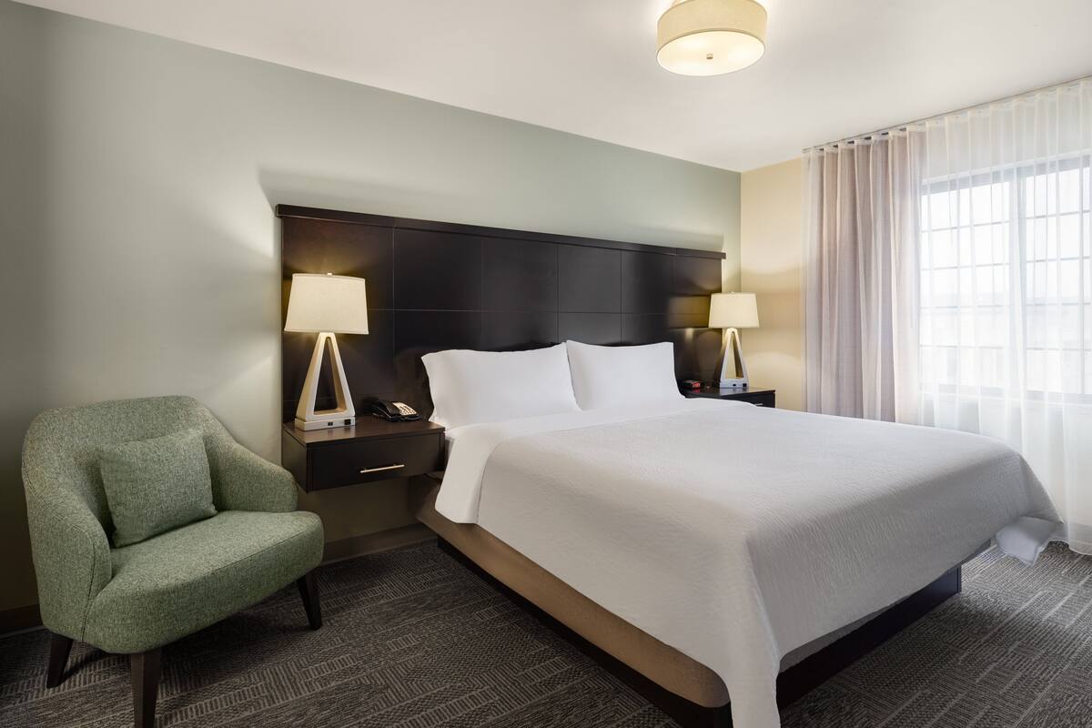 A hotel room with a bed, two bedside tables, a chair, and a ceiling light.