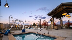 Un área de piscina con jacuzzi, sillones de descanso y una zona de estar cubierta con vistas a montañas.