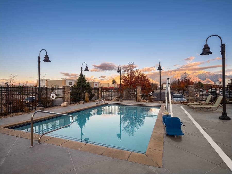 A pool area with a clear view of mountains in the background, surrounded by a fence and equipped with lounge chairs and a lifeguard stand.