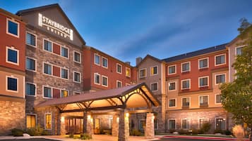 Un hotel Staybridge Suites con fachada de piedra, varias ventanas y un acceso cubierto.