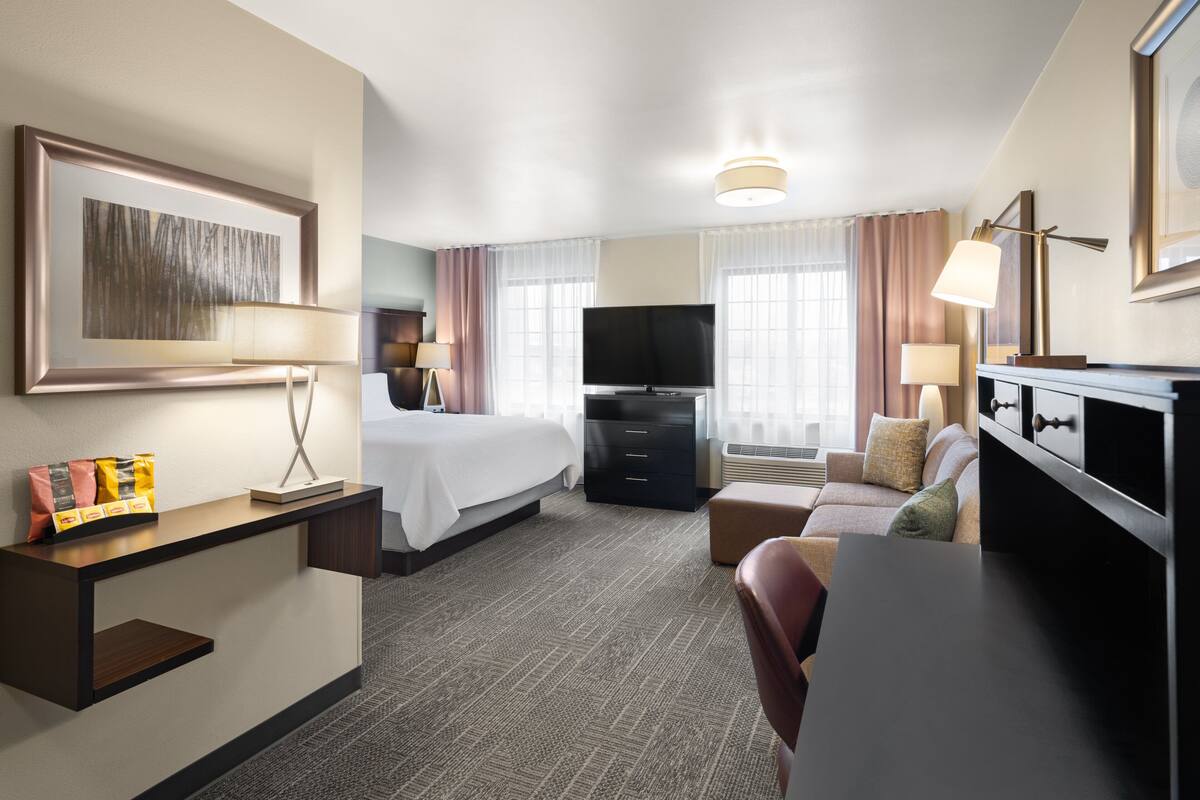 A hotel room with a bed, desk, TV, and seating area.