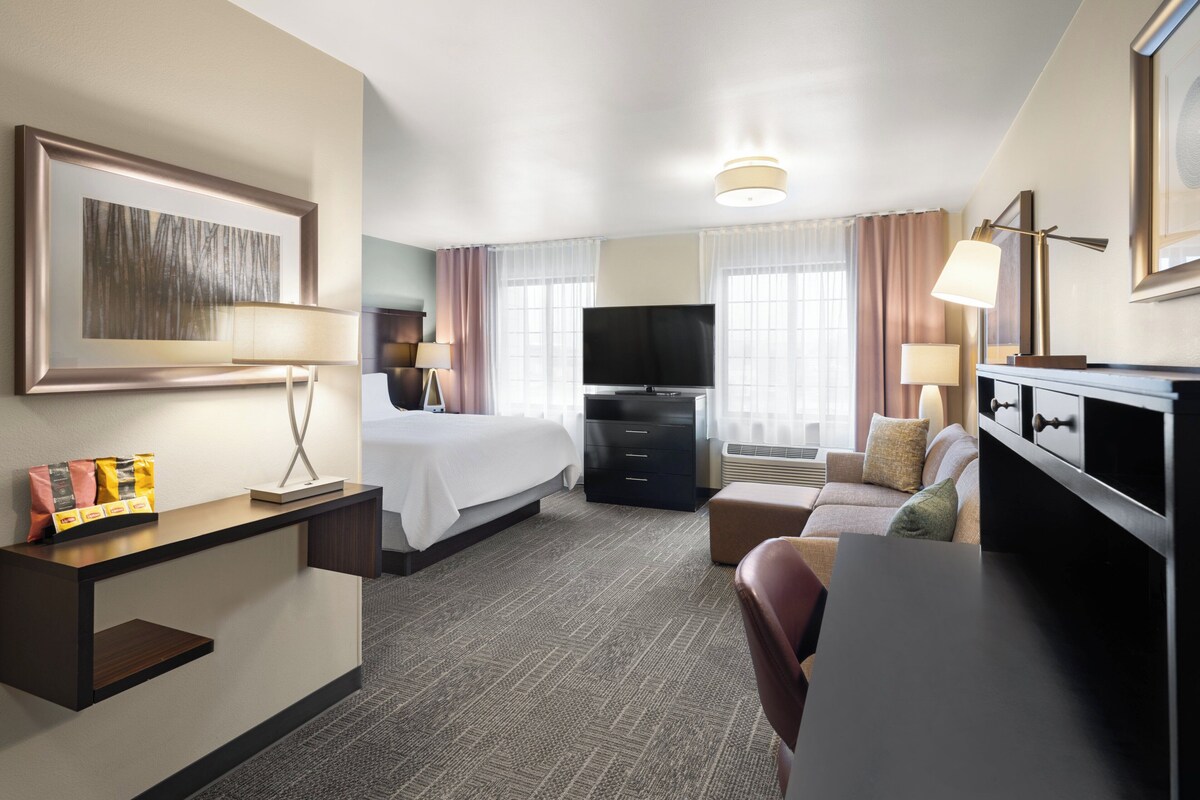 Habitación de hotel con cama, escritorio, televisor y zona de estar.