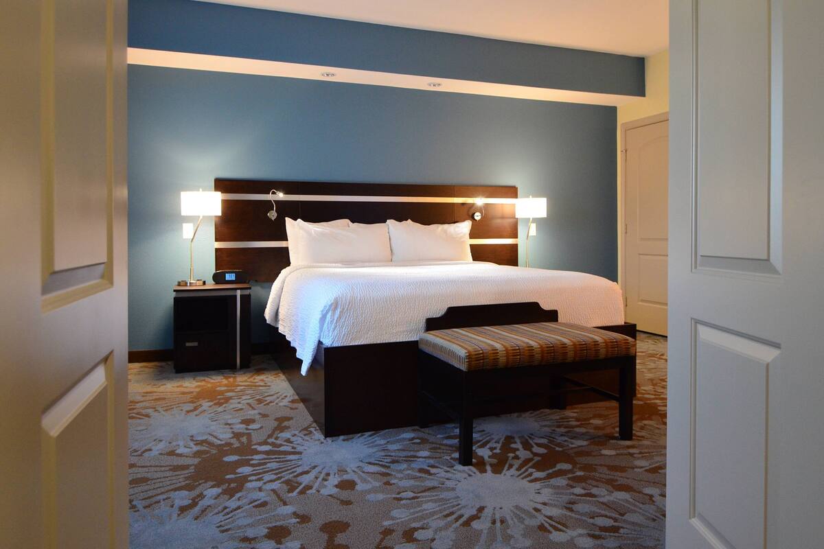 A hotel room with a large bed, bedside tables, and a bench.