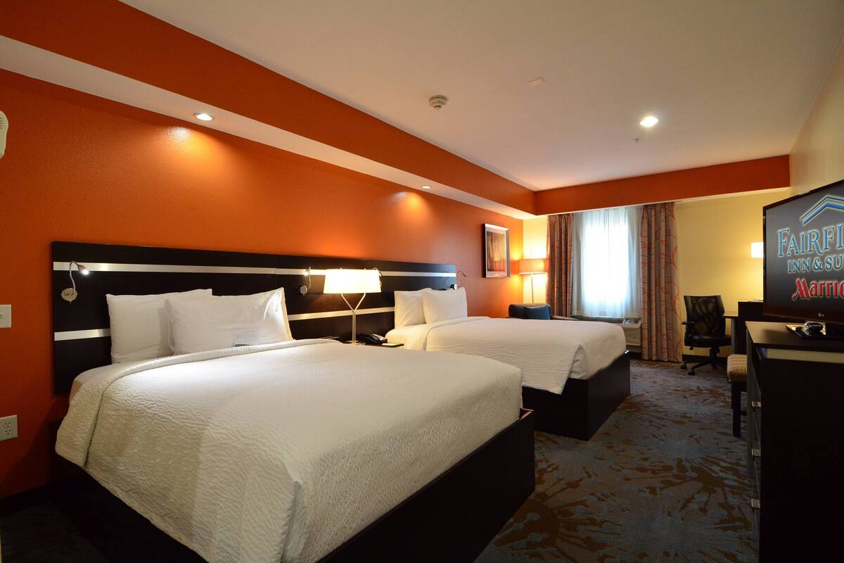 A hotel room with two beds, a desk, and a television.