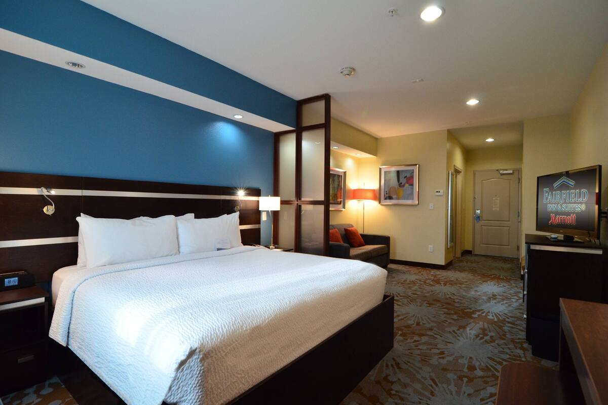 A hotel room with a large bed, a desk, a chair, a TV, and a door.