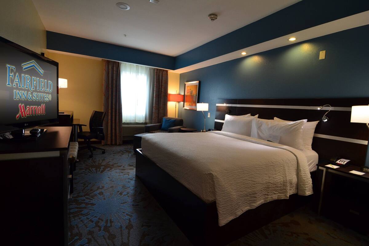 A hotel room with a large bed, a desk with a computer, a television, and a view of the outdoors.