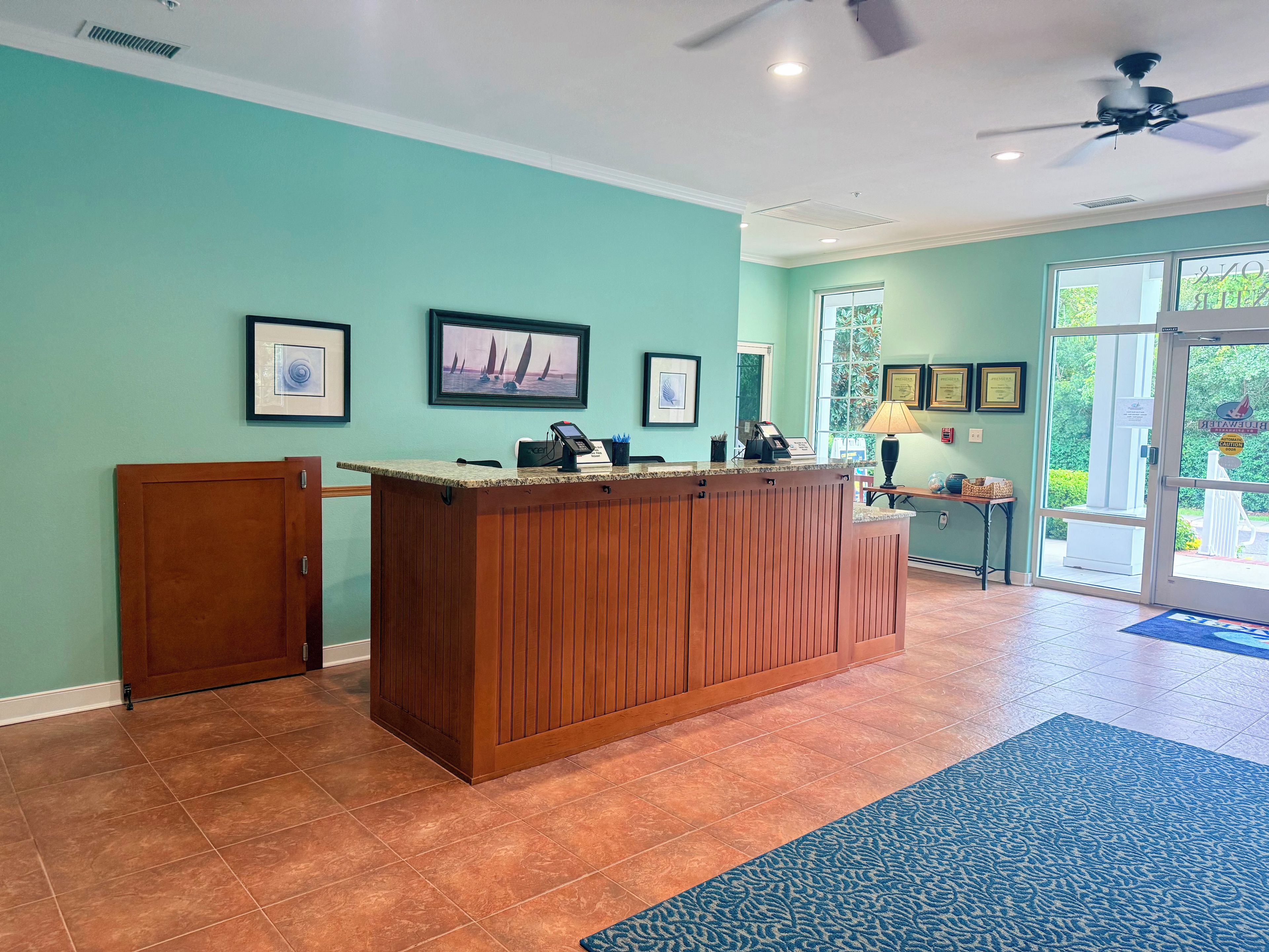 A reception area with a wooden counter, framed artwork, and a door leading outside.