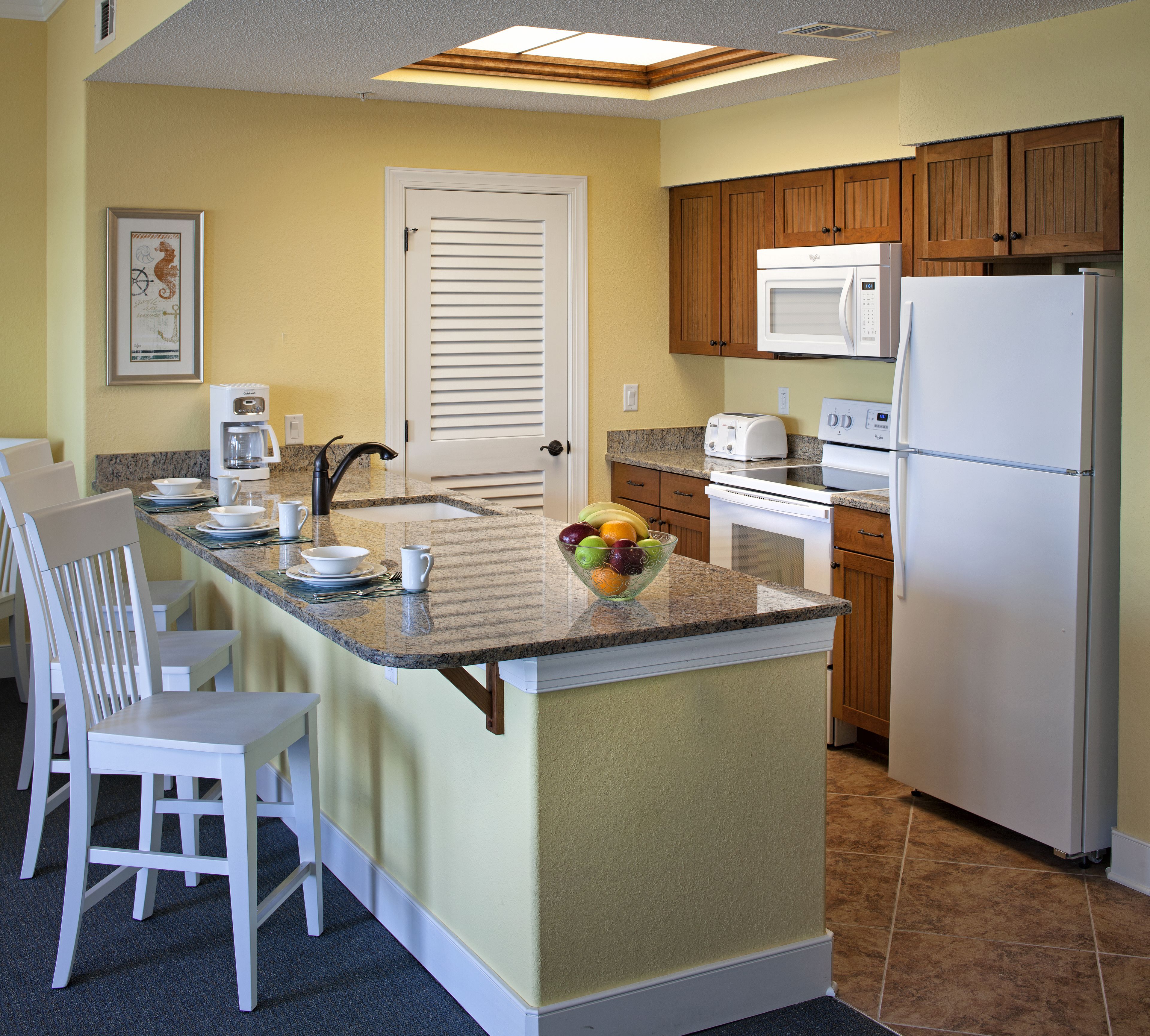 A kitchen with a central island, white appliances, wooden cabinets, and a framed picture on the wall.