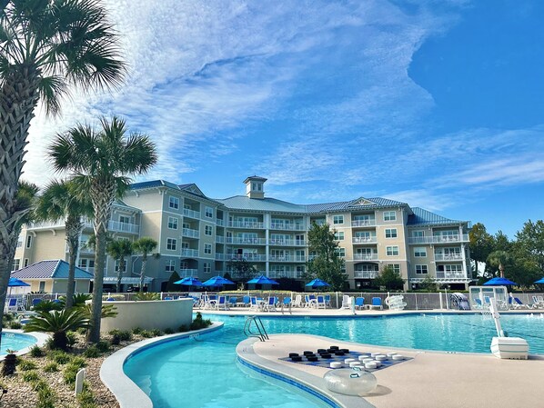 A resort with a swimming pool, palm trees, and a multi-story building with balconies.
