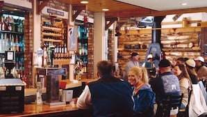A bar area with wooden shelves stocked with bottles, a cash register, and a television screen. - Snowcrest (Snowshoe)