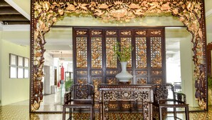 An ornate room with a traditional wooden partition, a central table with chairs, and a vase with a plant. - Museum Hotel (George Town)