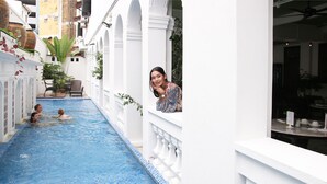 A narrow swimming pool with a tiled edge, surrounded by white walls and columns, with people swimming and a person leaning on the wall. - Museum Hotel (George Town)