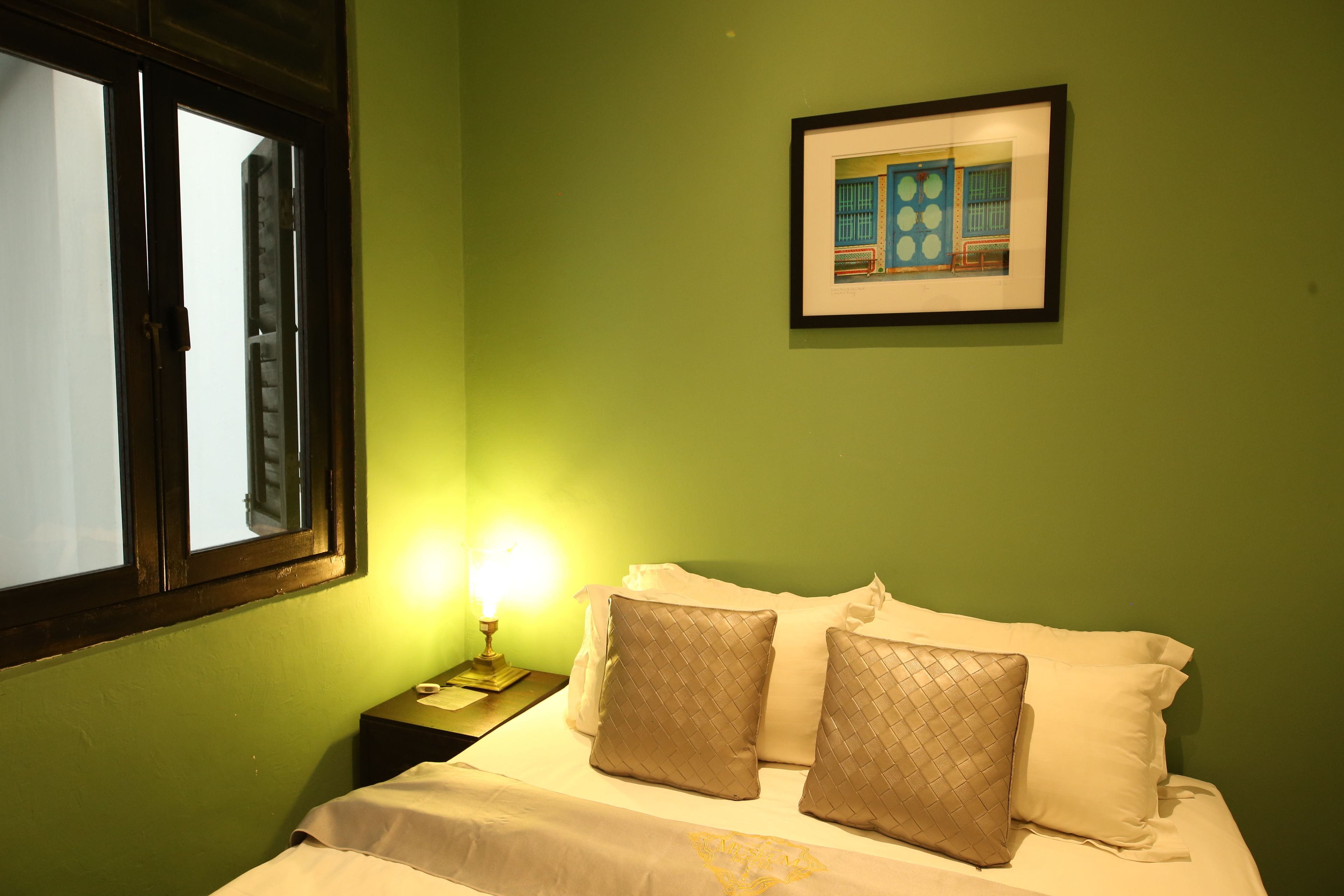 A room with a bed, a nightstand with a lamp, a framed picture on the wall, and a window with blinds.