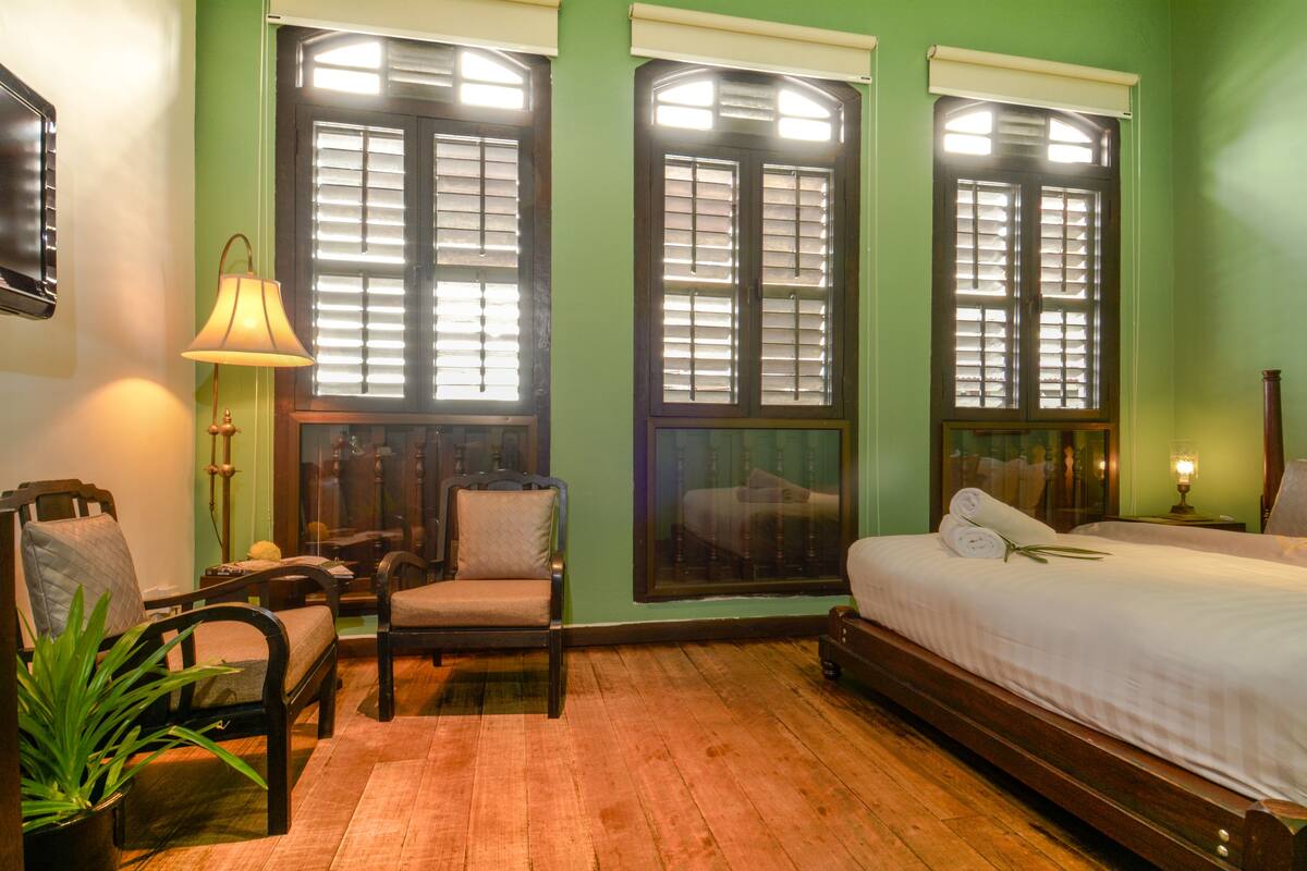 A room with a bed, two chairs, a lamp, and a potted plant.