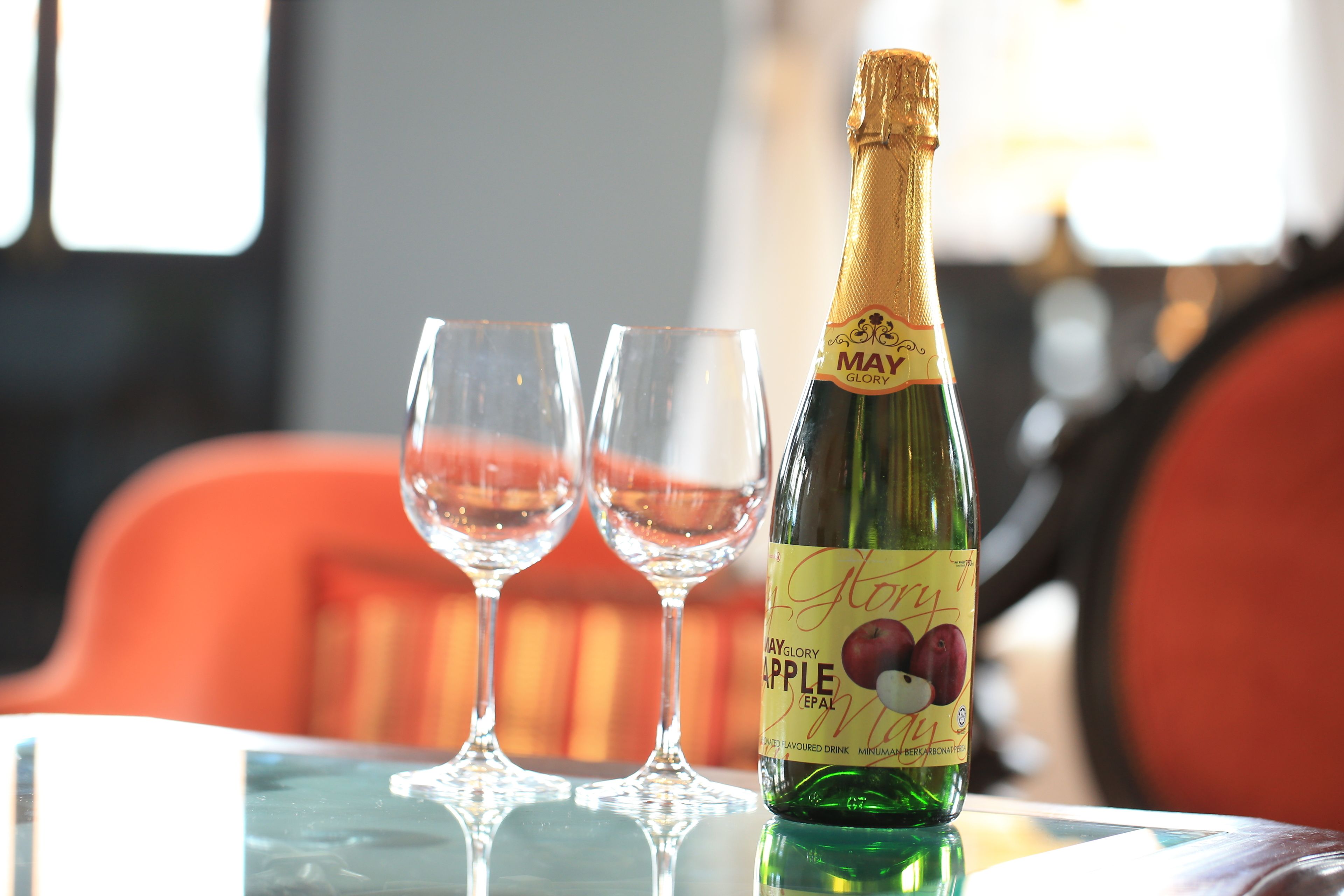 A bottle of May Glory Apple wine on a table with two empty glasses.