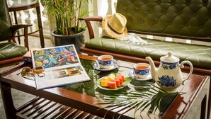 A cozy seating area with a green cushioned sofa, a wooden coffee table with a magazine, a teapot, cups, and a plate of fruit. - Museum Hotel (George Town)