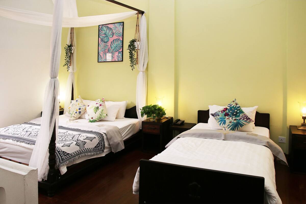 A bedroom with two beds, a canopy bed, and a bedside table with a lamp.