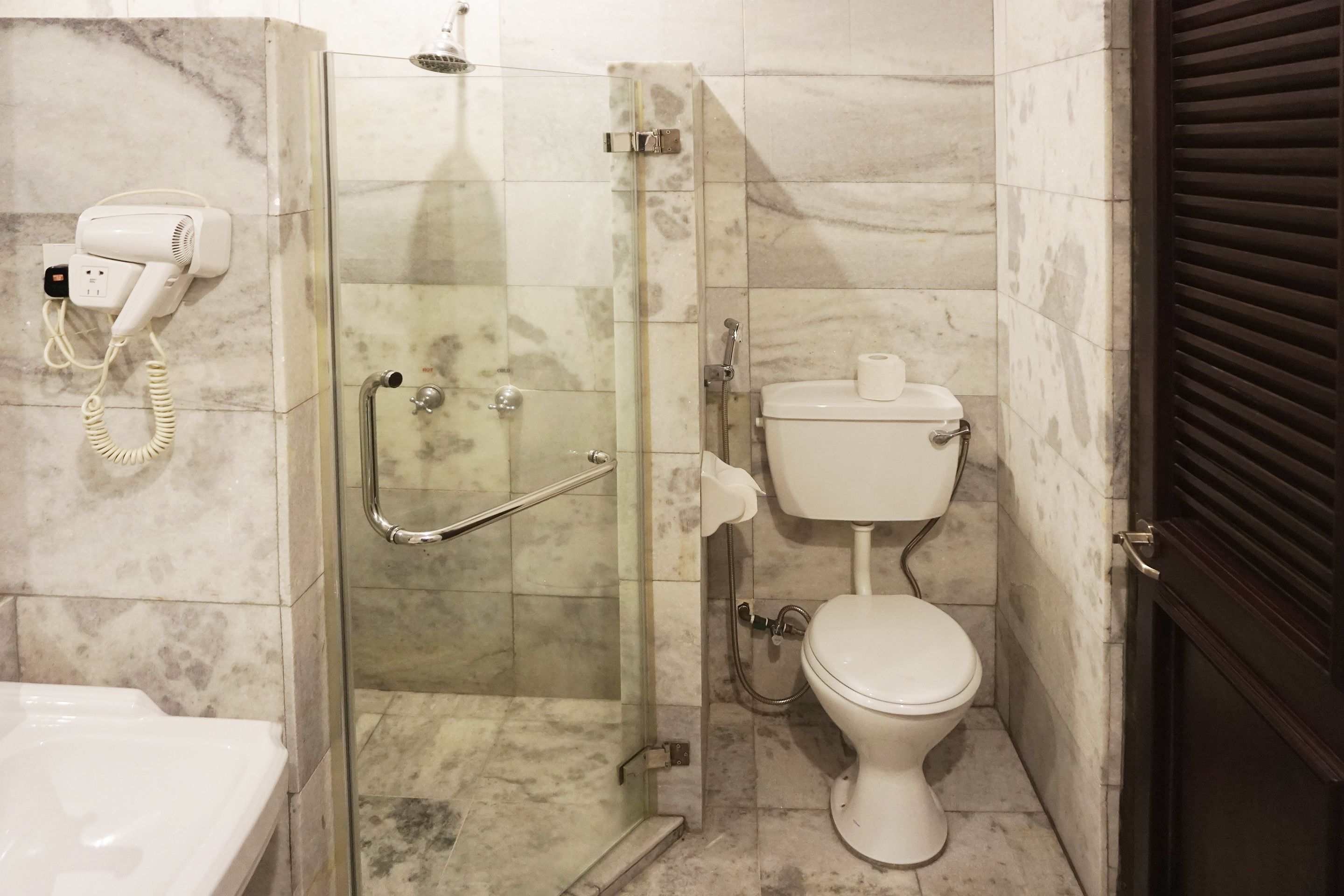 A bathroom with a glass-enclosed shower, a toilet, and a hairdryer on a wall socket.