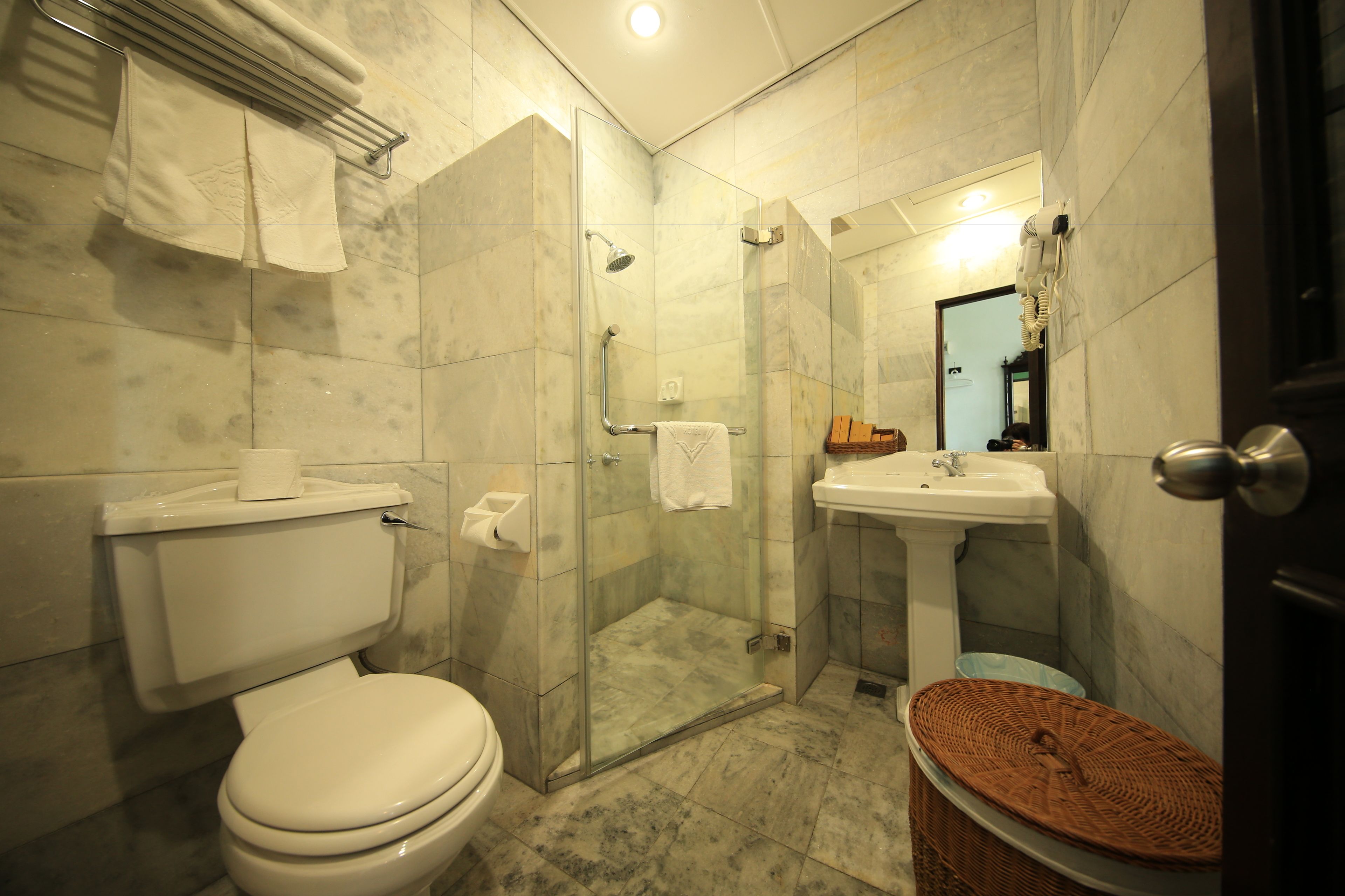 A bathroom with a toilet, a glass-enclosed shower, a sink, and a wicker basket.