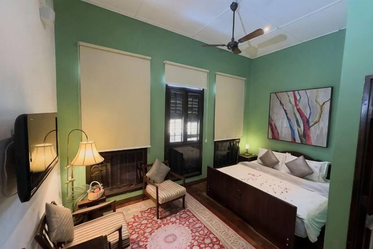 Une chambre à coucher avec un lit, une chaise, une lampe, une cheminée et un tableau.
