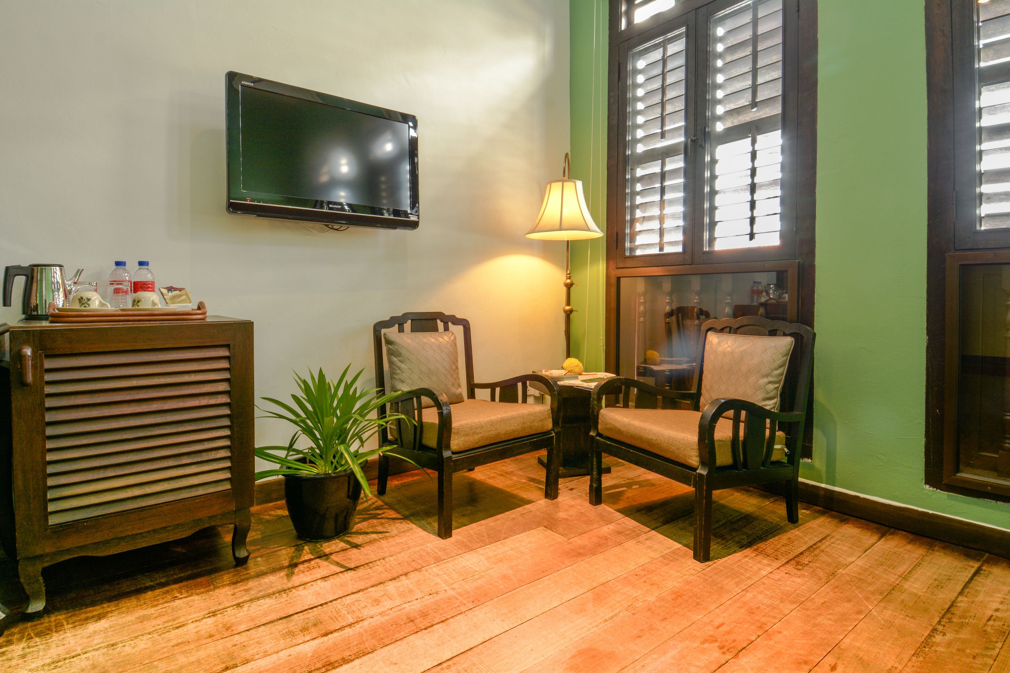 A room with a television mounted on the wall, a table with chairs, a potted plant, and a lamp.