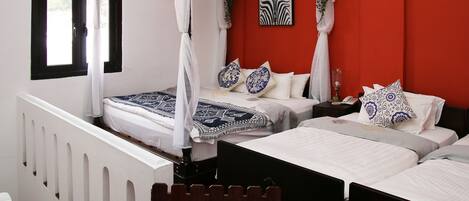 A bedroom with two beds, a red accent wall, a zebra print artwork, and a white canopy bed.