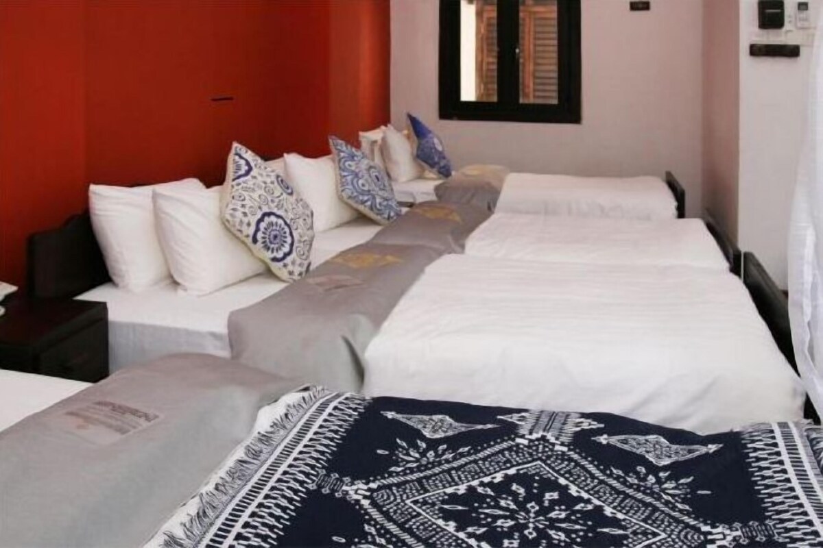 A hotel room with a red accent wall, a bed with patterned pillows, and a window with blinds.