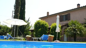 A swimming pool with lounge chairs and umbrellas, surrounded by greenery and a building. - Agriturismo da Lorena (Manciano)