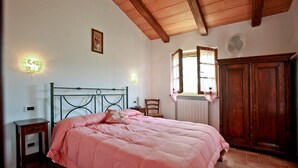 A bedroom with a bed, a wooden wardrobe, a nightstand, a wall-mounted light, and a window with curtains. - Agriturismo da Lorena (Manciano)