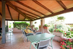An outdoor patio with a wooden pergola, green metal tables and chairs, a brick barbecue grill, and potted plants. - Agriturismo da Lorena (Manciano)