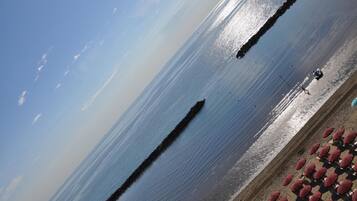 Ein Strand mit blauem Himmel, ruhigem Wasser und einer Reihe roter Sonnenschirme im Sand.