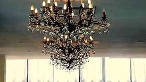 Un candelabro con múltiples luces tipo vela, un ventanal con vistas y una mesa con sillas.
