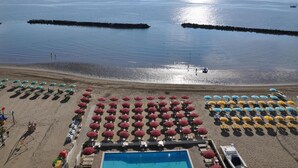 Un complejo turístico en la playa con hileras de sombrillas y tumbonas, una piscina y vistas al mar.