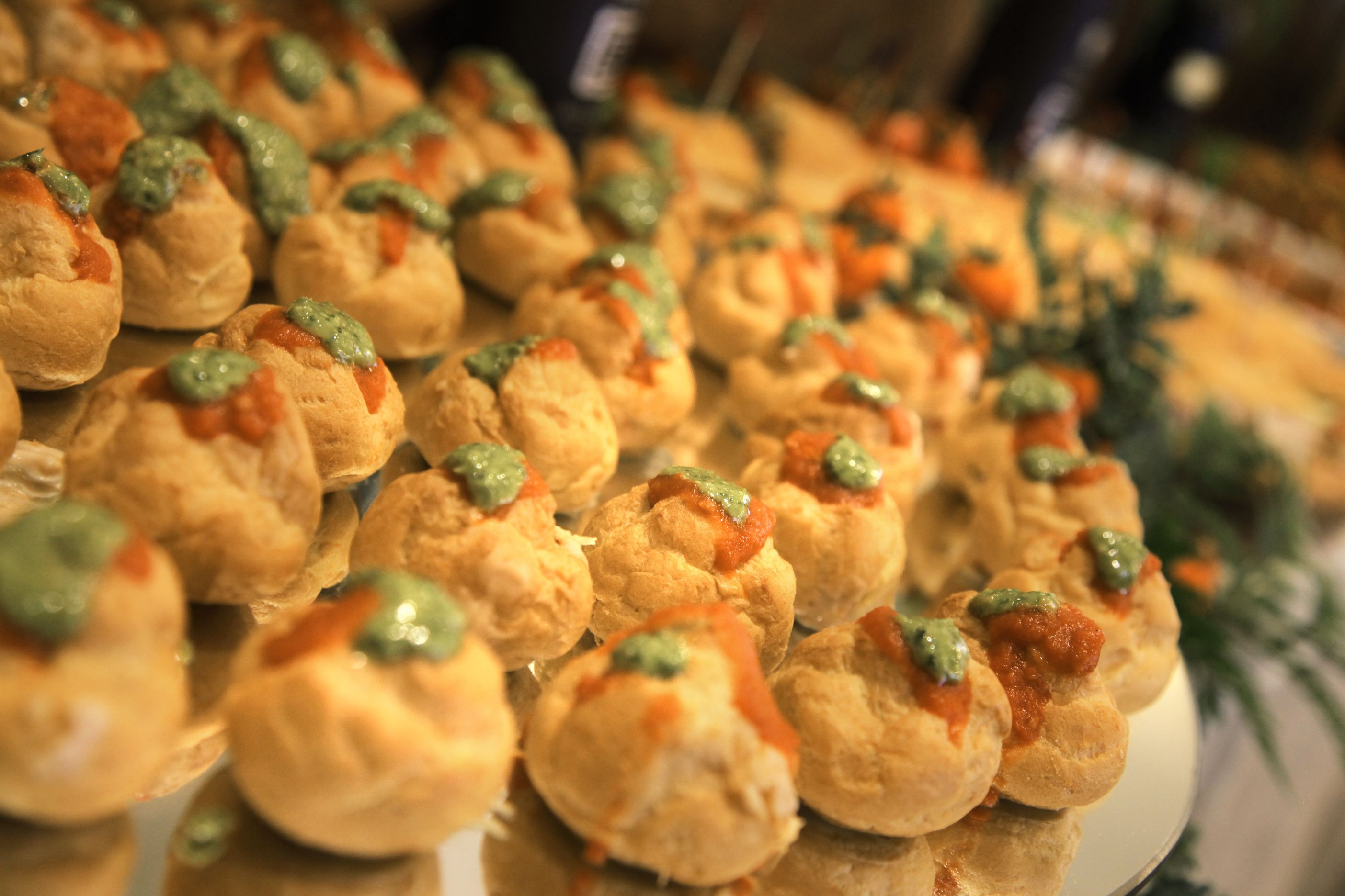 Primer plano de una exhibición de comida con pequeñas pastas cubiertas de salsas verdes y rojas.