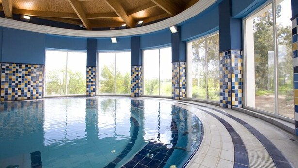 Una piscina interior con techo curvo y grandes ventanales.