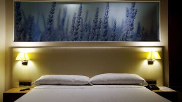 Habitación de hotel con una cama grande, dos lámparas de noche, una mesita de noche y un cuadro colgado en la pared con lavanda.