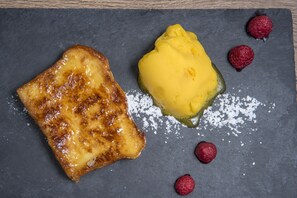 A dessert plate with a slice of cake, a scoop of ice cream, and raspberries on a slate surface. - El Raposo (Puebla de Sancho Perez)