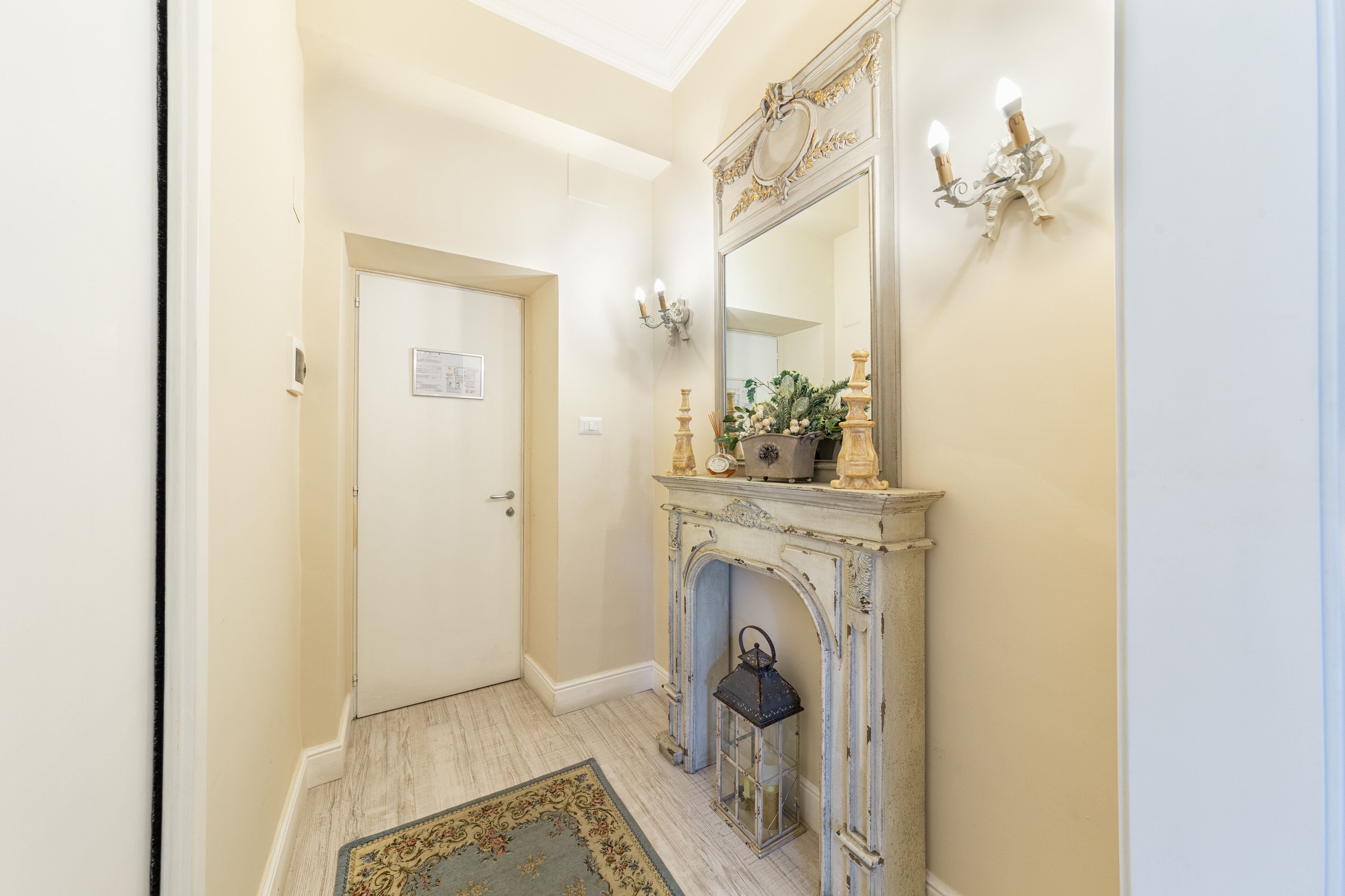 A hallway with a white door, a fireplace with a mirror above it, and a small lantern on the floor.