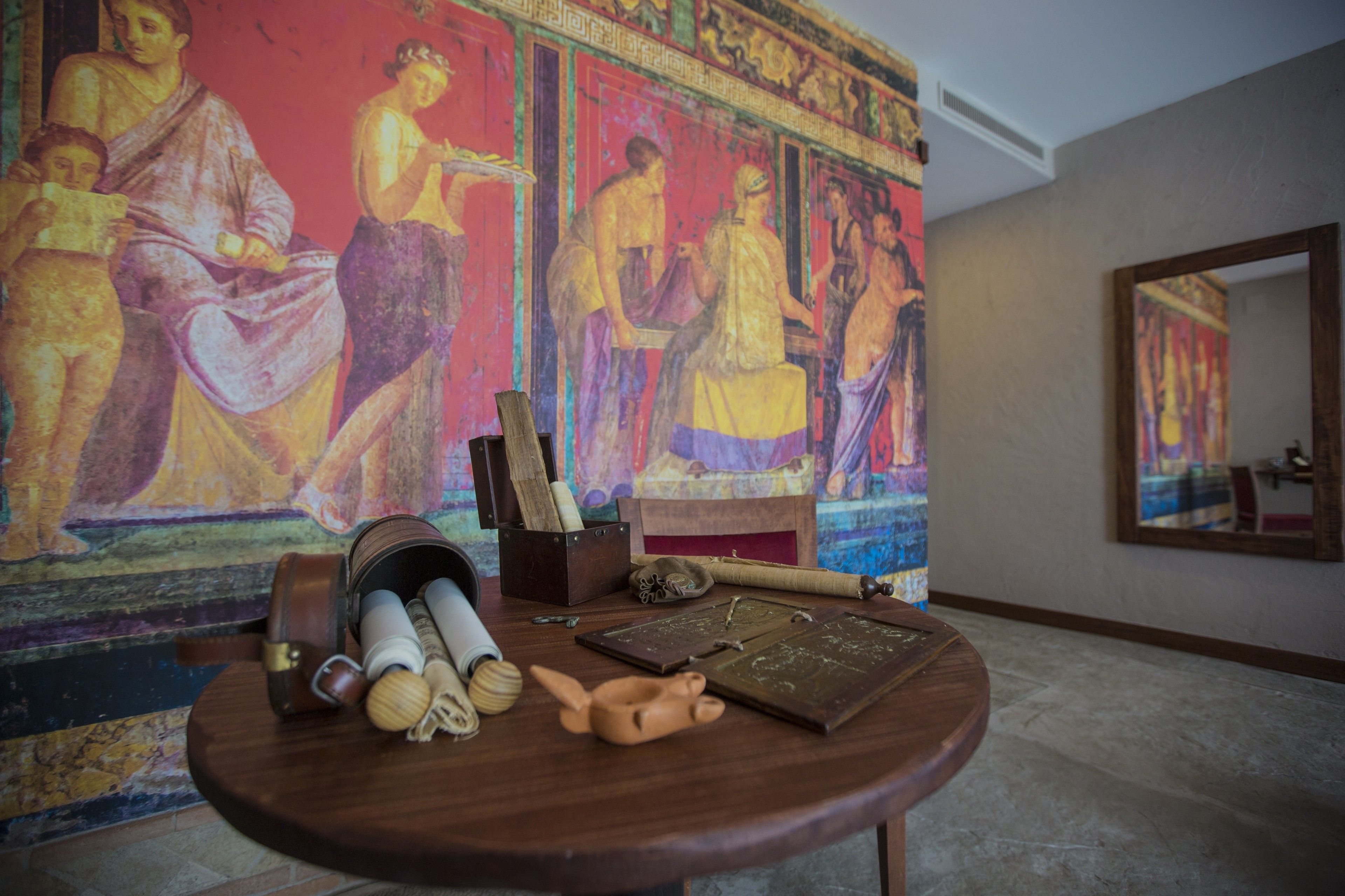 Een kamer met een grote muurschildering, een houten tafel met verschillende voorwerpen, en een spiegel.