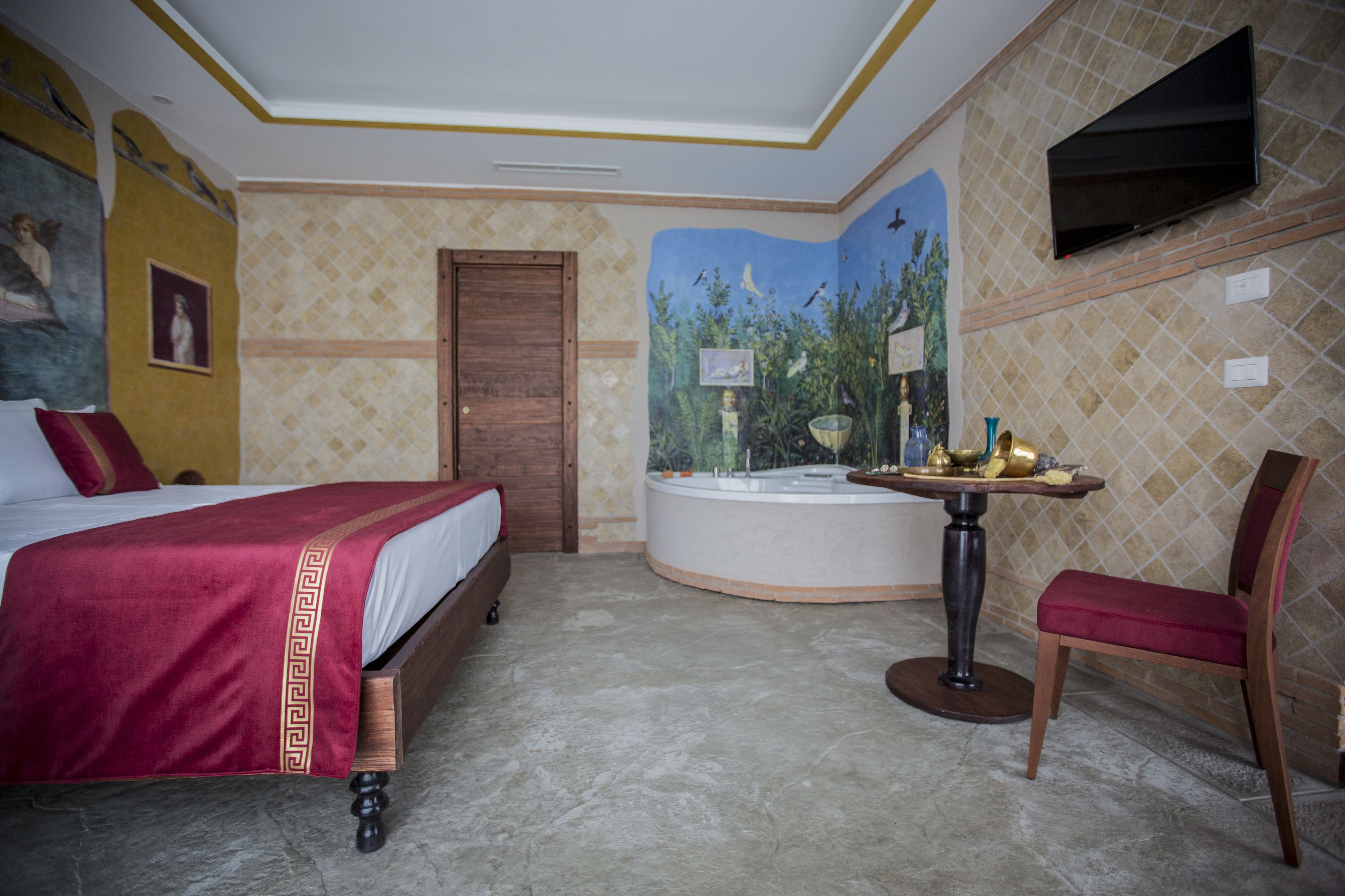 A hotel room with a bed, a round table with a chair, a bathtub, and a TV mounted on the wall.
