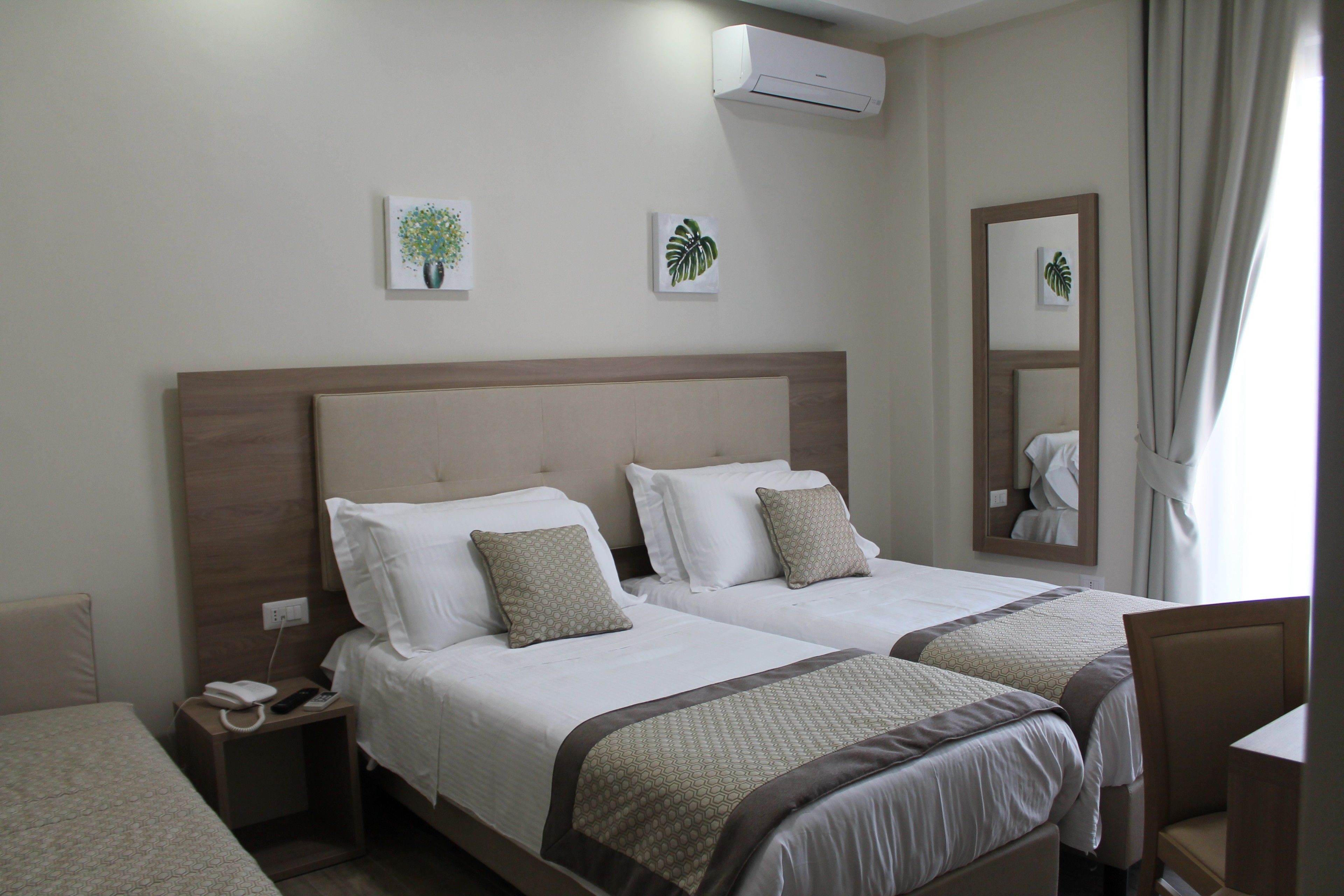 A hotel room with two beds, a nightstand, a chair, and a mirror.
