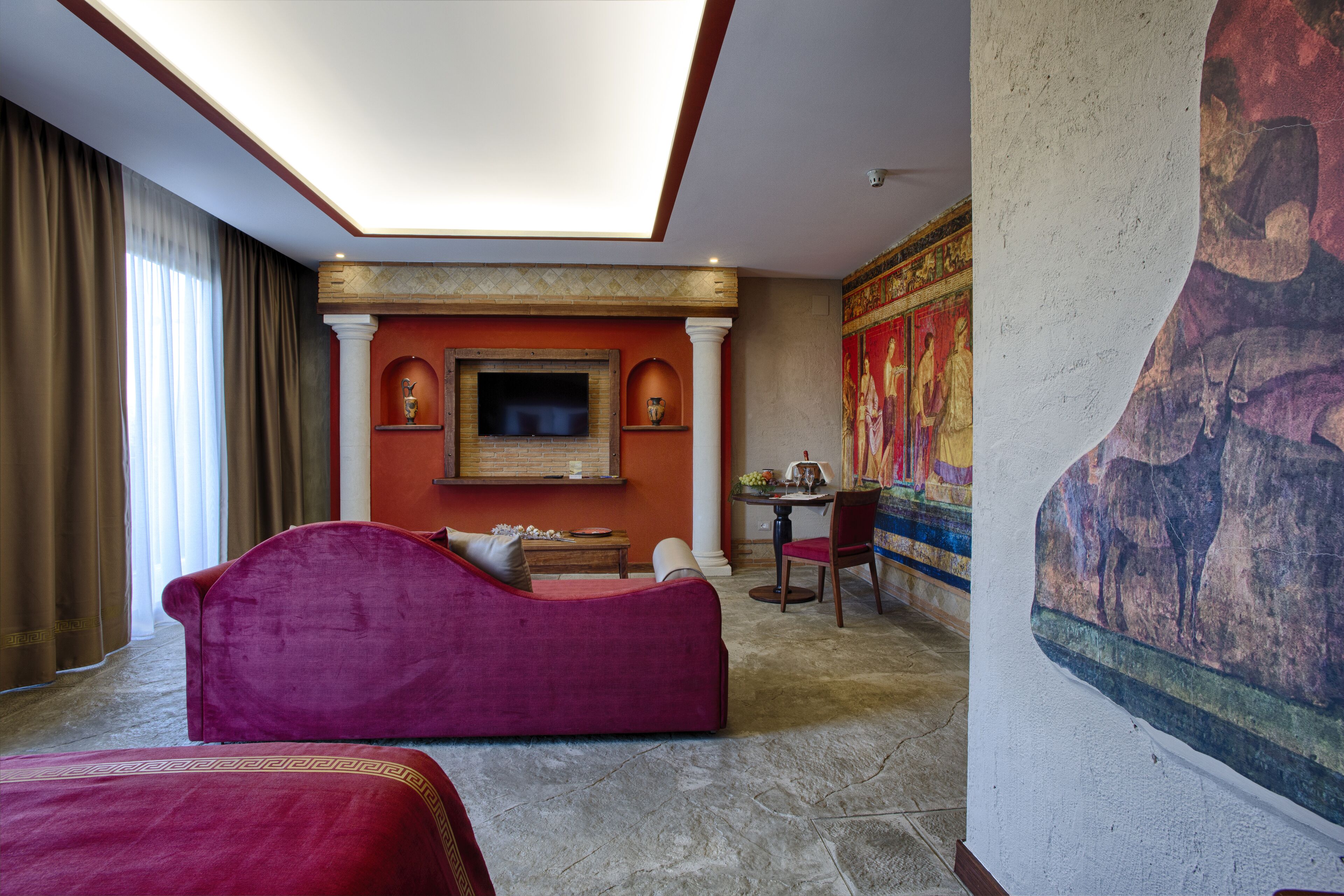 A hotel room with a large bed, a television, a dining table, and a mural on the wall.