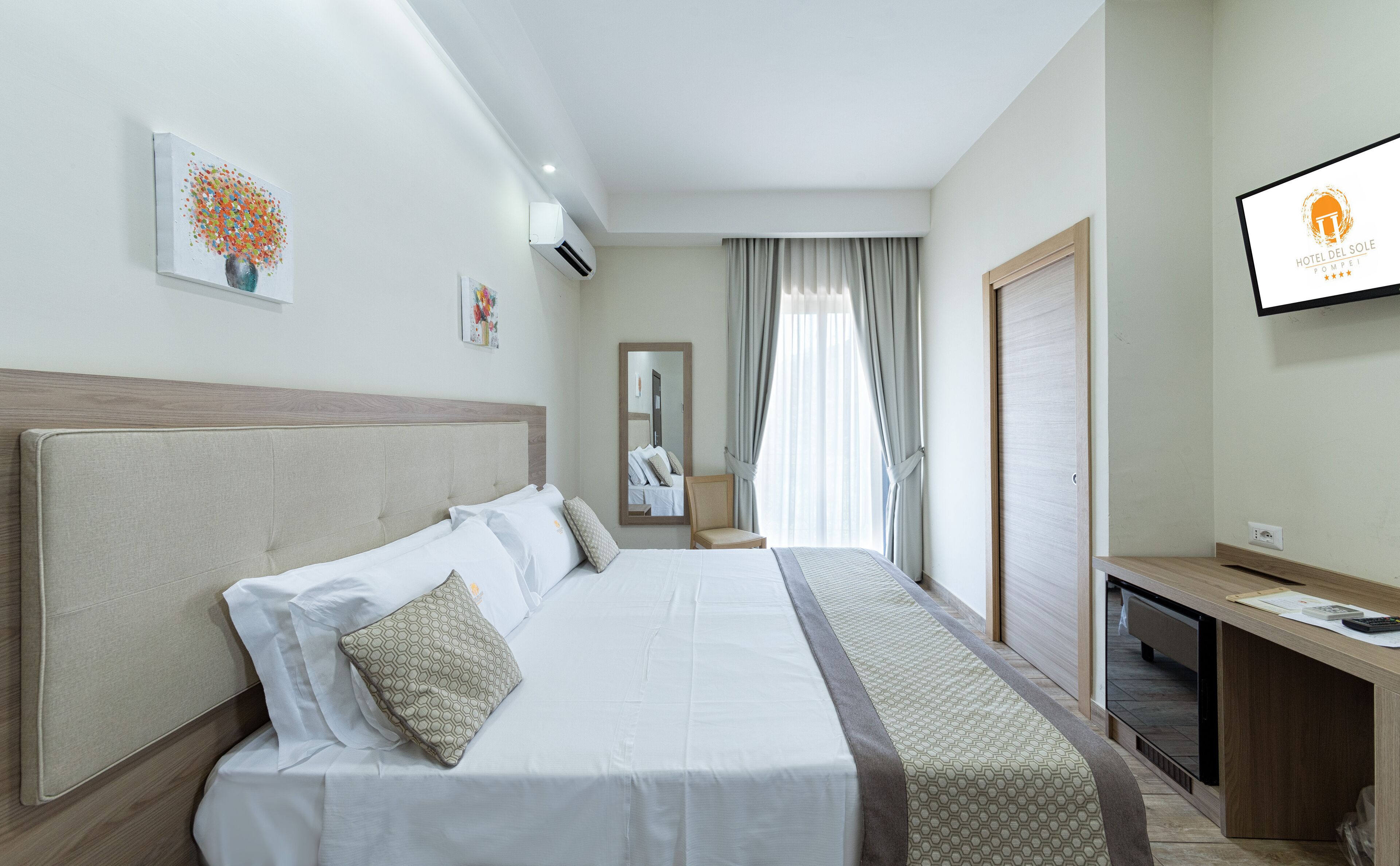 A hotel room with a large bed, a desk, a TV, and a mirror.