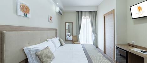 A hotel room with a large bed, a desk, a TV, and a mirror.