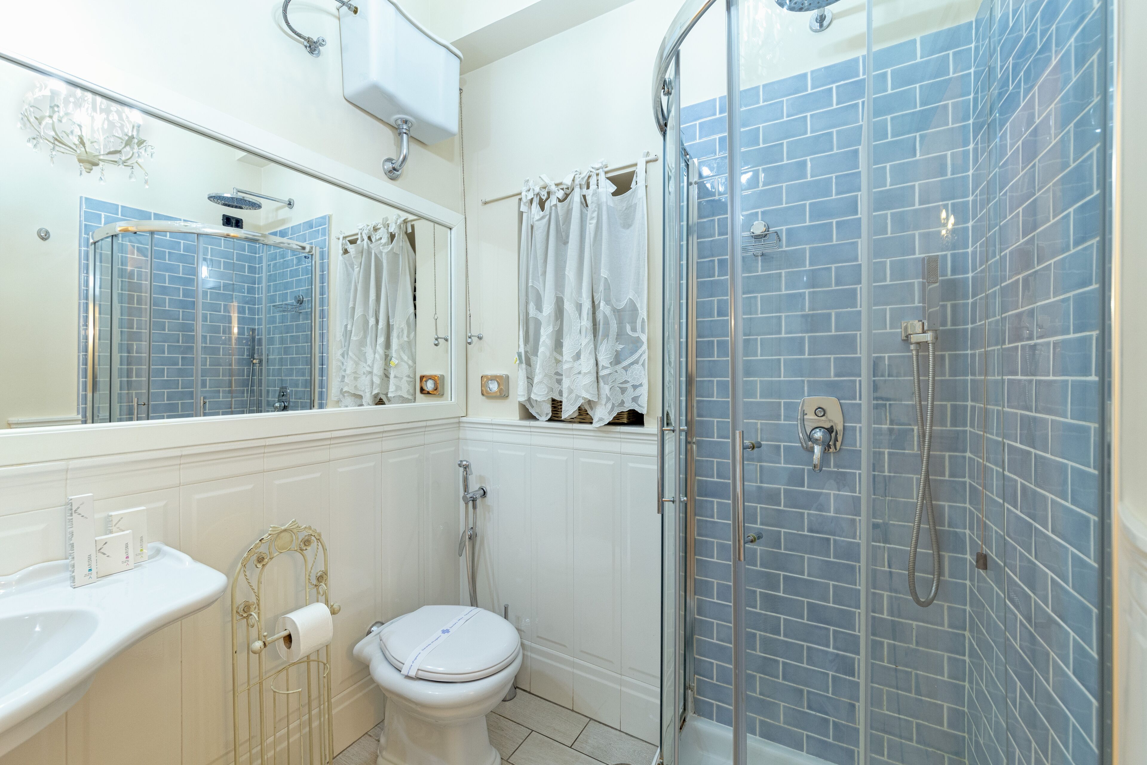 A bathroom with a white toilet, a sink, a shower with a glass door, and blue-tiled walls.