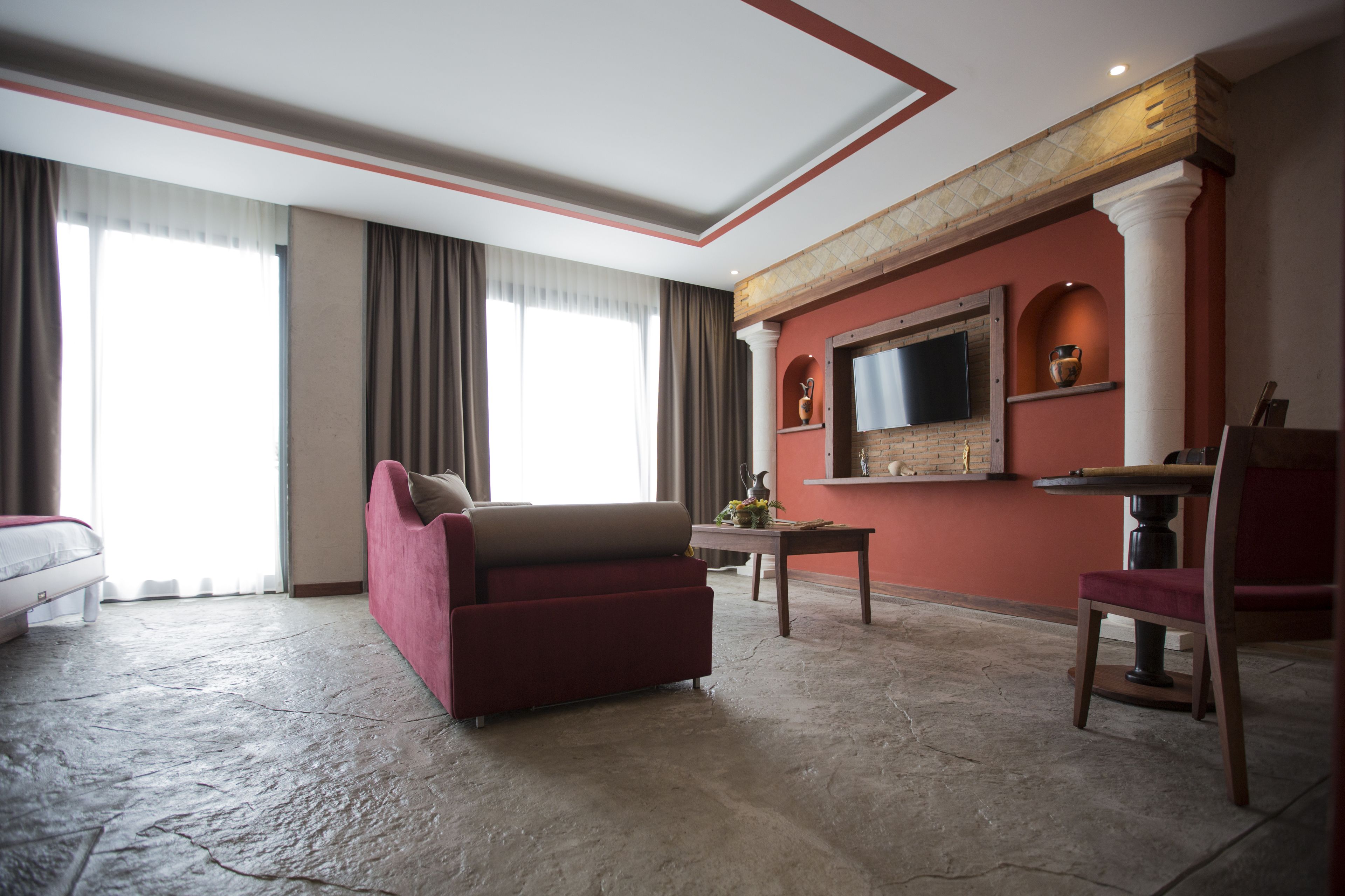 Quarto de hotel com uma cama grande, um sofá vermelho, uma mesa de madeira e uma TV na parede.
